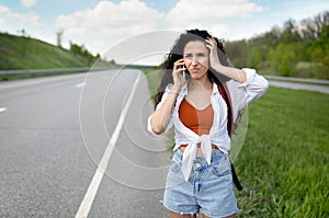 Confused young woman standing along road, feeling lost, calling on smartphone, checking travel options outdoors