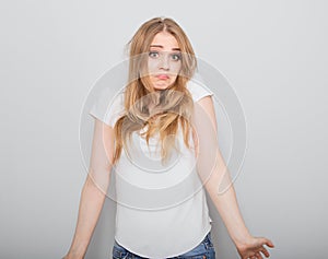 Confusion very offended fair blond hair woman thinking, looking sad and spreading her hands. Casual neutral shirt clothing on grey