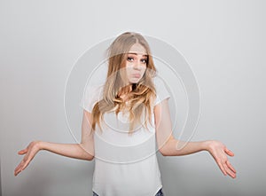 Confusion very offended fair blond hair woman thinking, looking sad and spreading her hands. Casual neutral shirt clothing on grey