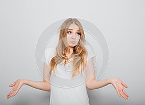 Confusion very offended fair blond hair woman thinking, looking sad and spreading her hands. Casual neutral shirt clothing on grey