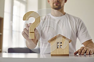 Confusion young man who is hesitant about buying his home shows wooden question mark.