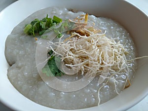 Congee with offal in white bowl topping with fried noodles.