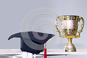 Congratulate graduate.Trophy and black hat on background.
