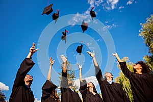 Congratulations! Low angle view of happy group of six young cheerful multi ethnic graduates in black gowns are throwing up their