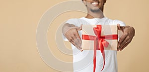 Smiling young african american man in white t-shirt giving gift box with present with red ribbon