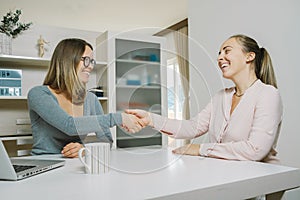 Congratulations! Two female shaking hands with smile while sitting at the office with laptop