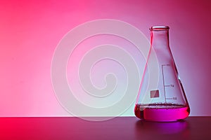 Conical flask with liquid on table against color background