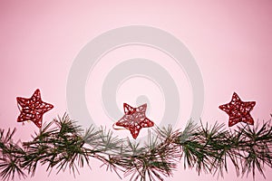 Coniferous branches and red stars - Christmas tree decorations on a New Year`s pink background, copy space