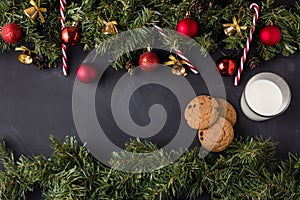 Coniferous Christmas garland decorated with red balls and golden bells with caramel canes at the top and bottom of the black table