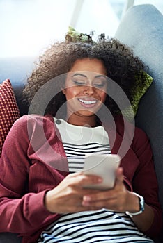 Connect with good company. a young woman using a mobile phone while relaxing on the sofa at home.