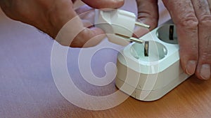 Connect the power cable. A male hand connects an electric cord to an extension cord. Close up of a white electric plug connected t