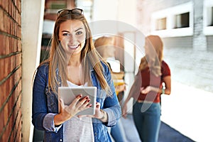 Connected between classes. Shot of a smiling female university student standing on campus using a digital tablet with