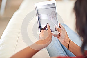 Connected on the couch. High angle shot of a young woman using her tablet while relaxing at home.