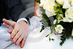 Connected hands of happy newlyweds without ring with bridal bouquet