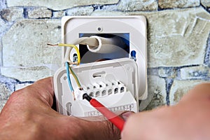 Connecting wires to wall thermostat for floor heating system, an electrician uses crosshead screwdriver for installation