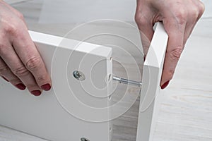 The woman inserts the part into the white furniture panel of the photo