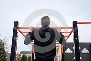 Conportative young man making pull-up exercises on the crossbar outdoors. Back view. Fitness, sport, exercise, training and