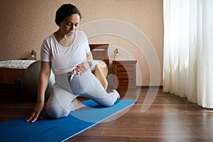 Conscious pregnant woman touching her belly while performing leg-split during prenatal stretching exercises on yoga mat
