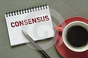 CONSENSUS - word in a white notebook on a gray background with a pen and a cup of coffee