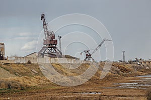 Consequences of Aral sea catastrophe. Abandoned port with rusty cranes on the shore of dried Aral sea