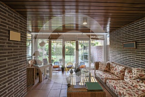 A conservatory overlooking a backyard with gardens and grass and wicker and rattan furniture
