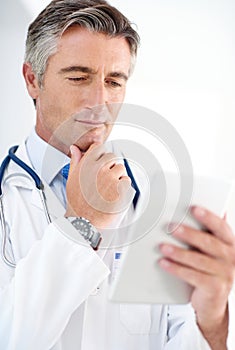 Considering his treatment options. a doctor holding a digital tablet while standing in a hospital corridor.