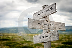 consistency builds trust text engraved on old wooden signpost outdoors in nature