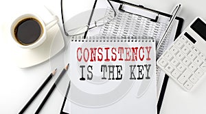 CONSISTENCY IS THE KEY text on the paper with calculator, notepad, coffee ,pen with graph