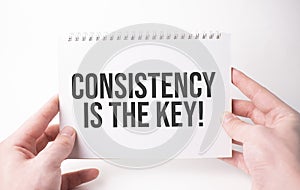 Consistency is the key word inscription on white card paper sheet in hands of a man. Black letters on white paper. Business