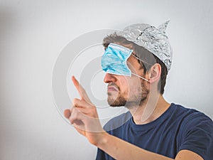 Conspiracy theory concept: Young angry man wearing aluminum hat and face mask over the eyes is gesturing angry