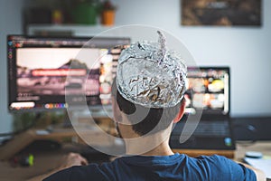 Conspiracy theory concept: young man is wearing aluminum head, sitting in front of the pc watching videos