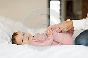 Constipation in babies. Caring mother doing gymnastics to child girl lying on bed, making massage to little daughter