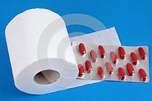 Constipation concept with toilet paper roll and laxative blister pack on blue background