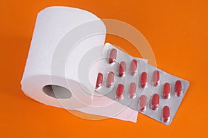 Constipation concept with toilet paper roll and laxative blister pack on orange background