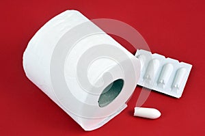 Constipation concept with toilet paper roll and suppositories on red background