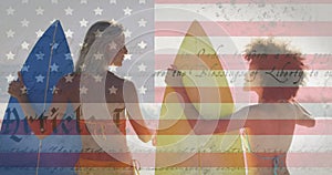 Constitution text over american flag against rear view of two women with surf boards at the beach