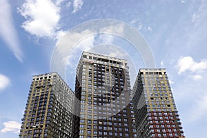 Constructing modern buildings with insulation on facades under beautiful sky with white clouds, conceptual photo