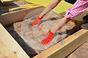 Constructing a rooftop a building contractor in protective gloves is lying glass wool batt insulation