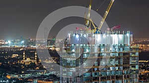 Construction activity in Dubai downtown with cranes and workers night timelapse, UAE.