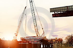 Construction of an automobile bridge with cranes and pouring concrete over the river in the rays of the setting sun