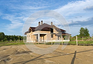 Construction of brick family house in suburbs. Shell of town home with completed walls and roof. Building a home in the field