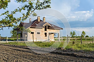 Construction of brick family house in suburbs. Shell of town home with completed walls and roof. Building a home in the field