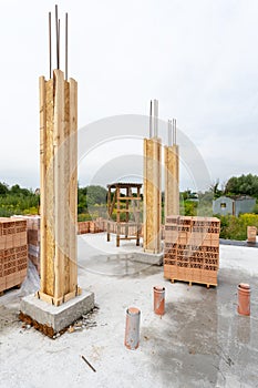 Construction of brick house concept. Vertical photo of few wooden and concrete column formwork standing outside on the foundation