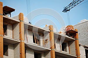 Construction of a brick residential building made of red and white bricks against a blue sky