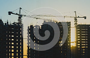 Construction of a building with cranes above sun in the background