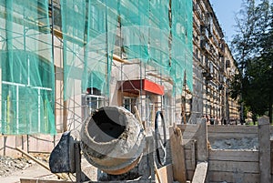 A construction concrete mixer stands near the building being repaired