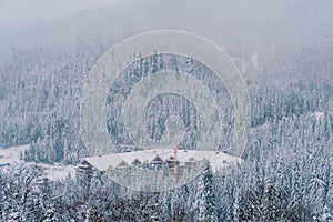 Construction crane above a snow-covered multi-story hotel in the middle of a forest in the mountains. Top view