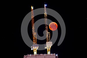 Construction crane on the background of a full red moon. Red moon, total lunar eclipse.