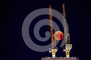 Construction crane on the background of a full red moon. Red moon, total lunar eclipse.