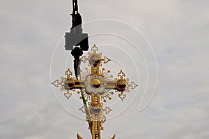 Construction crane with boom structure at construction site. The rise of the golden cross on the dome of the temple, gray cloudy